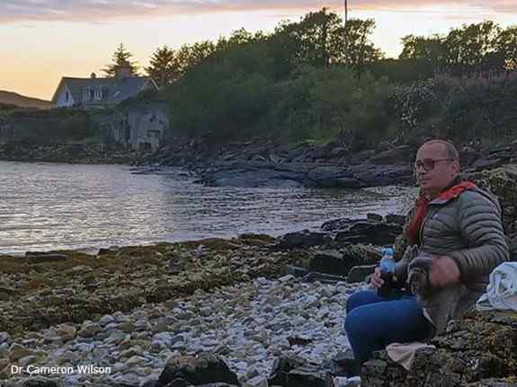 Dr Cameron Wilson, sitting by a Scottish lake
